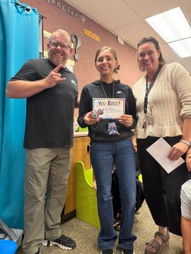 Three people posing in a classroom, holding a certificate and smiling at the camera.