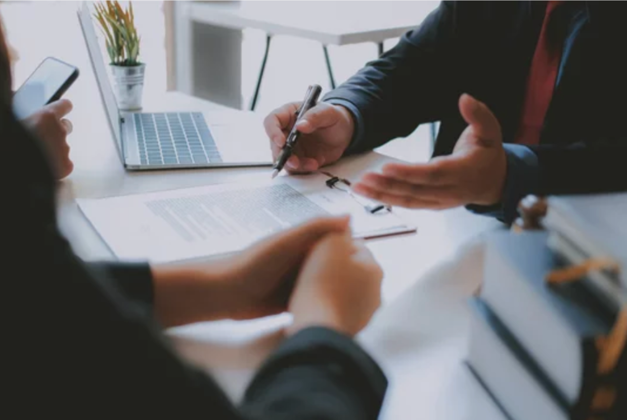 A professional close-up shot of a person in a suit signing a document while another person listens. 
