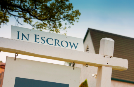 A close-up photo of a real estate “In Escrow” sign displayed outside a residential property. 