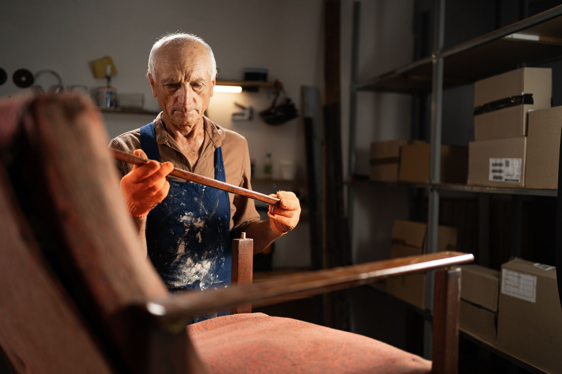 Man in hoodie uses a staple gun to reupholster a chair seat in a workshop.