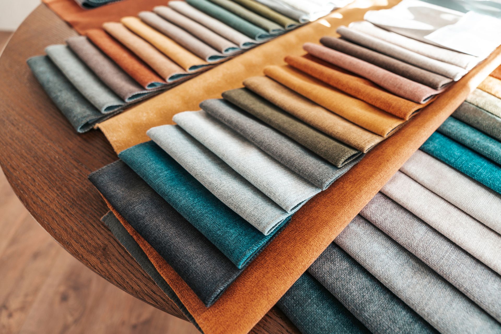 A collection of fabric swatches in various colors and textures, arranged in layers on a wooden table.
