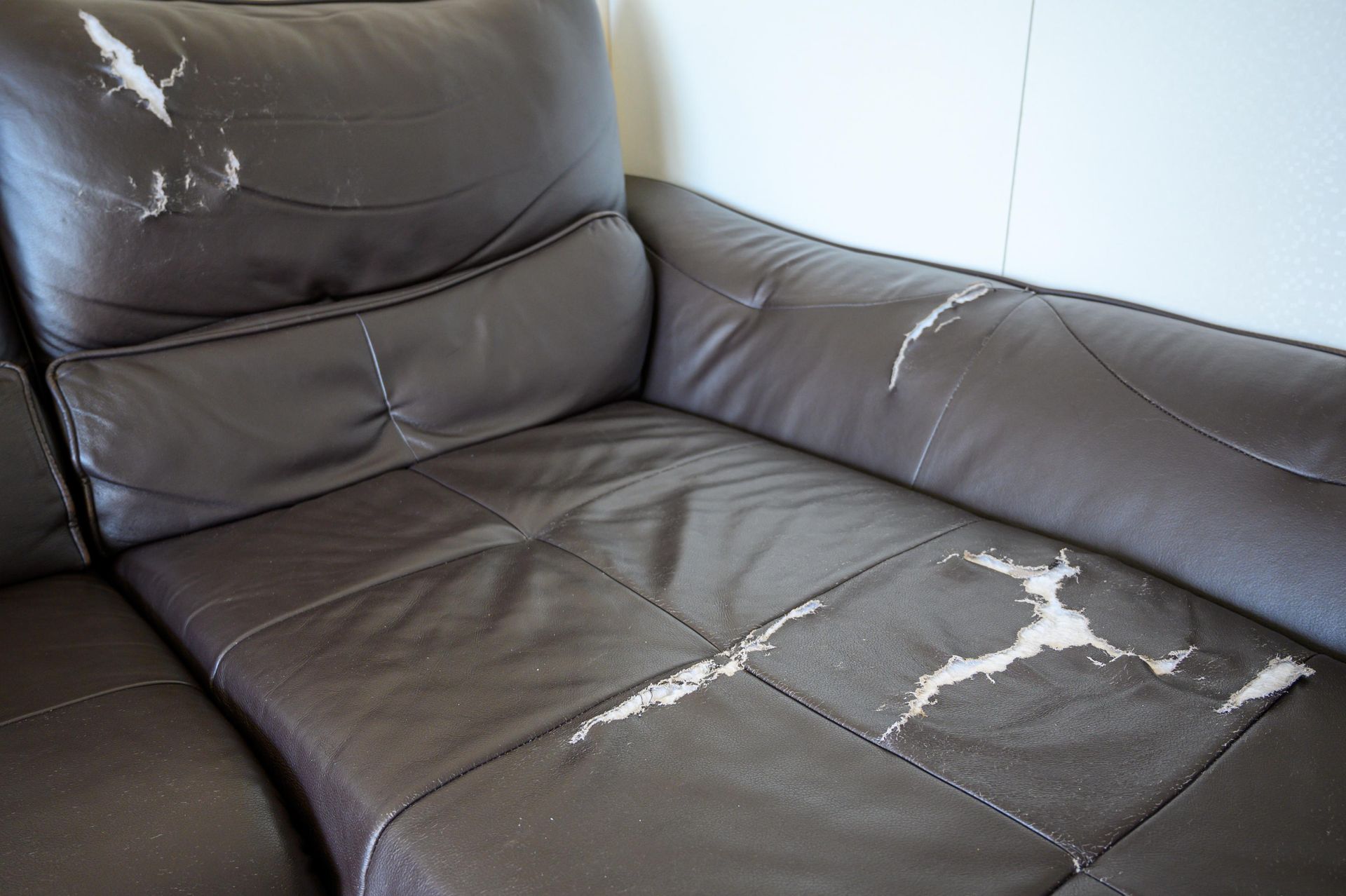 Damaged brown leather sectional sofa, torn and peeling in a room.
