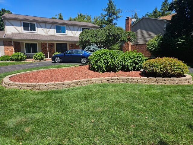 A house features a nicely landscaped centerpiece in the yard with wood chips and shrubbery