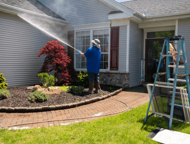 A man is using a soft power wash on the side of a house to clean it
