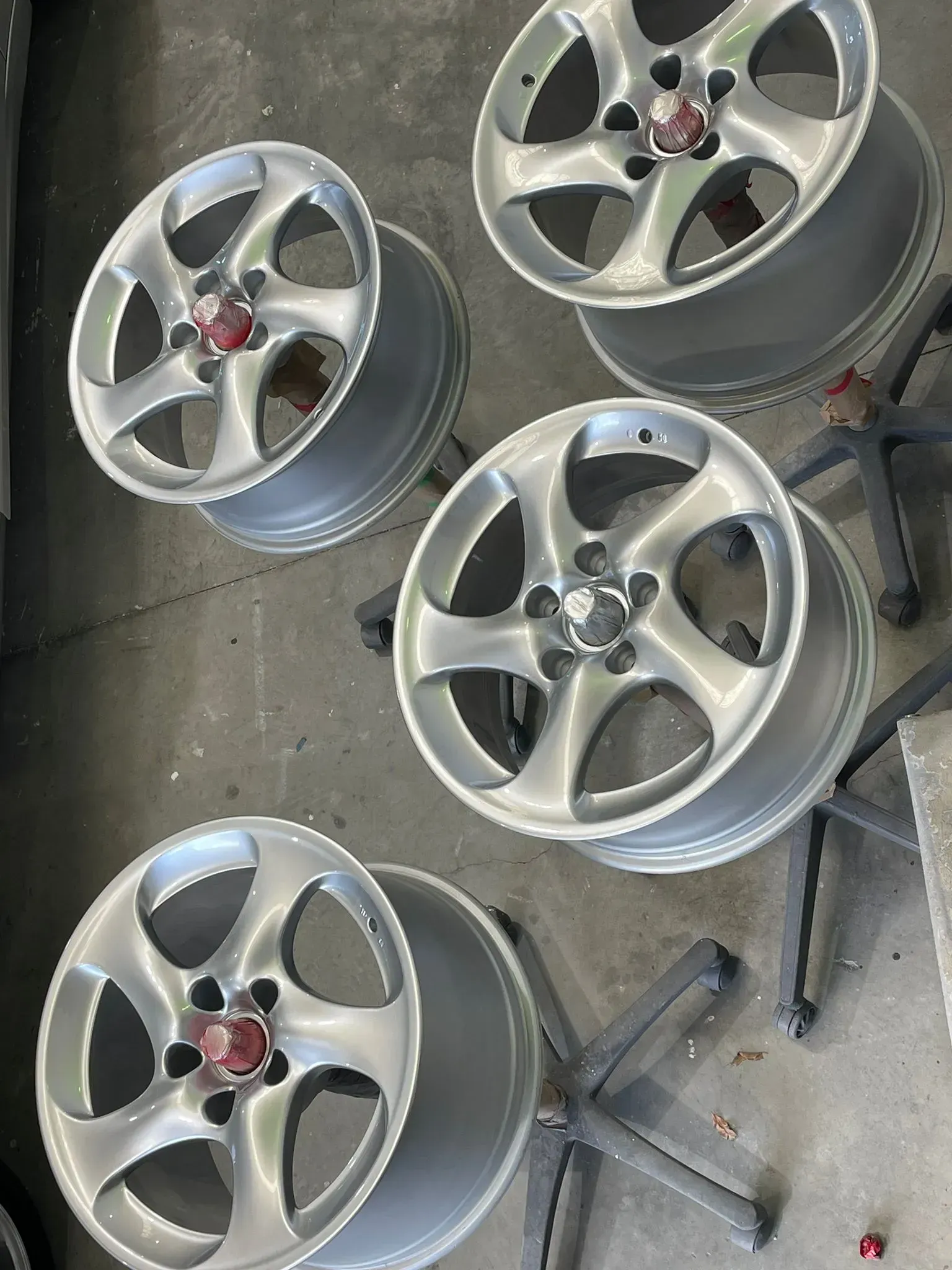 Five silver car wheels with red center caps on a gray surface, possibly a workshop.  — Coolum Smash Repairs in Coolum Beach, QLD