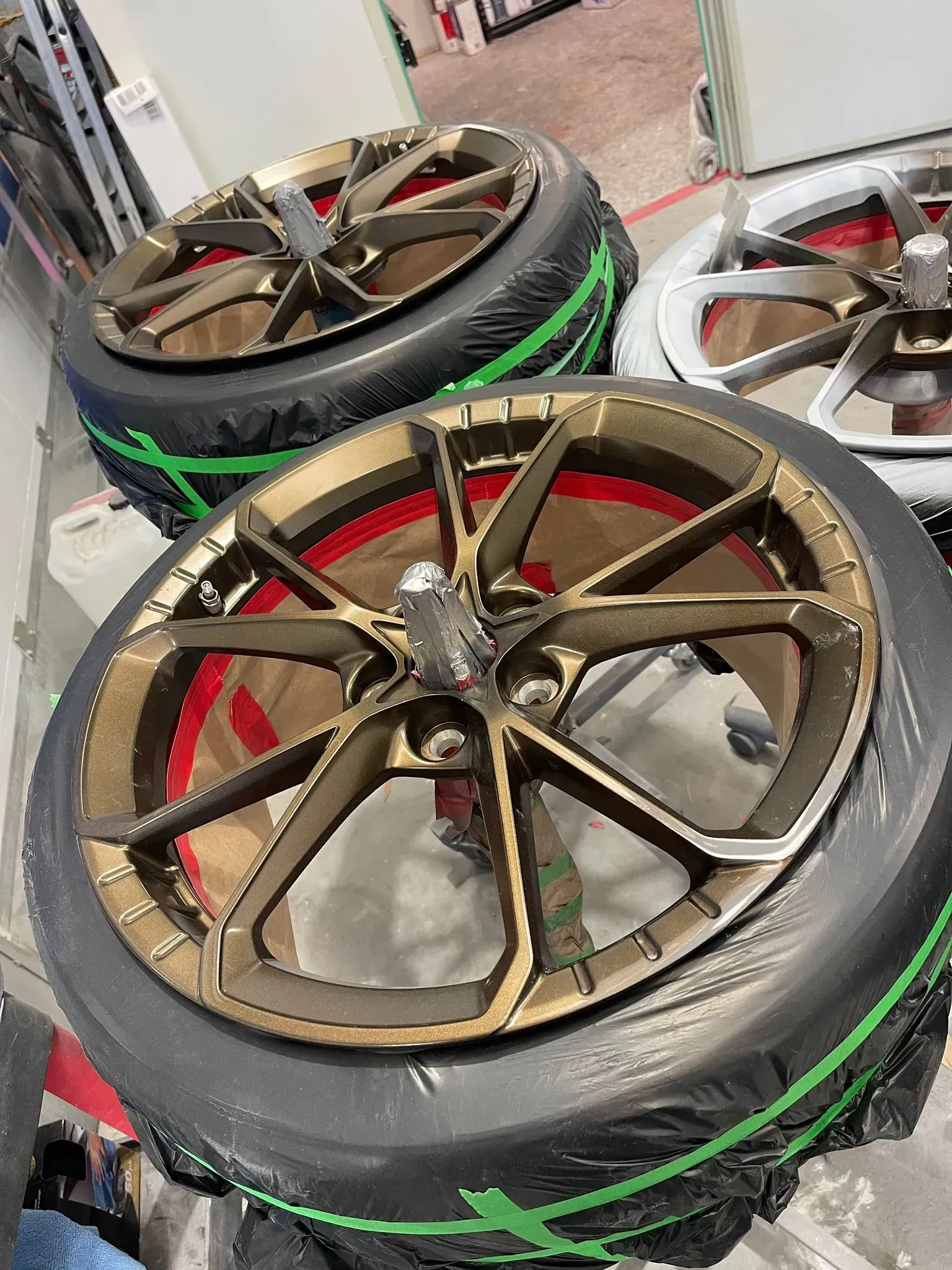 Three bronze alloy car wheels with tires, wrapped in black plastic, resting indoors. — Coolum Smash Repairs in Coolum Beach, QLD