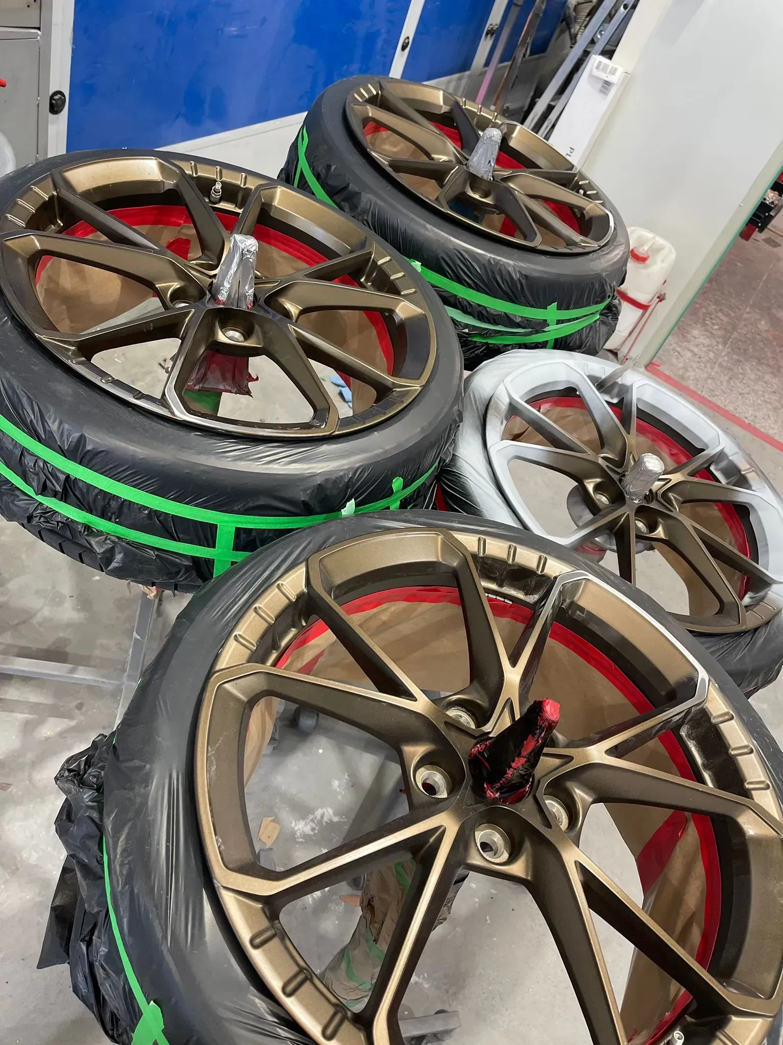 Four gold-coloured car wheels with red accents, and tires with green bands, in an indoor setting — Coolum Smash Repairs in Coolum Beach, QLD