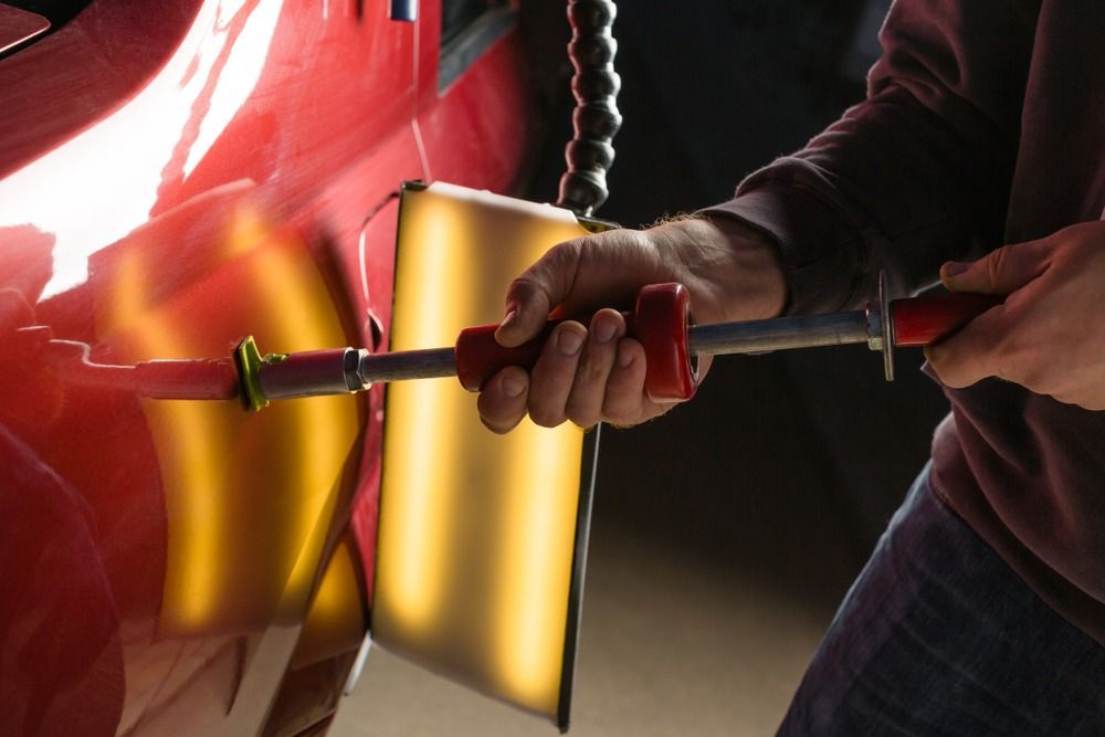 Person using a dent puller tool on a red car, illuminated by a light panel. — Coolum Smash Repairs in Coolum Beach, QLD