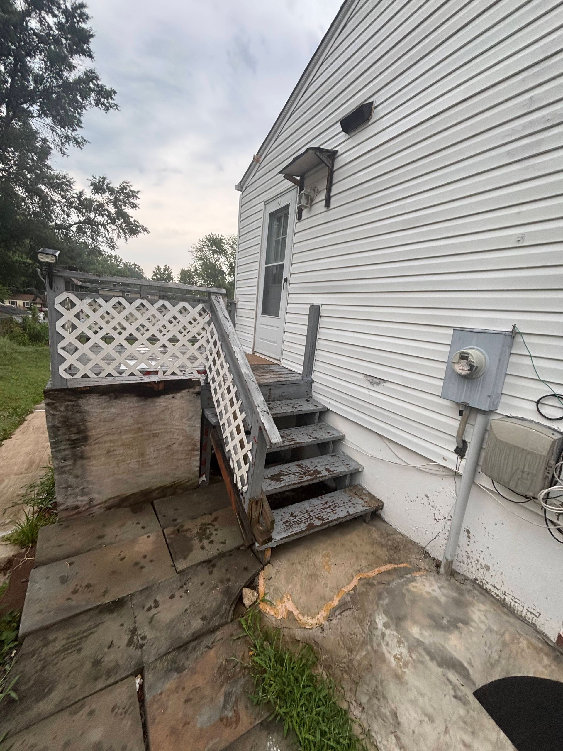 Steep exterior concrete steps beside a white house, with a small lattice railing and utility meter.