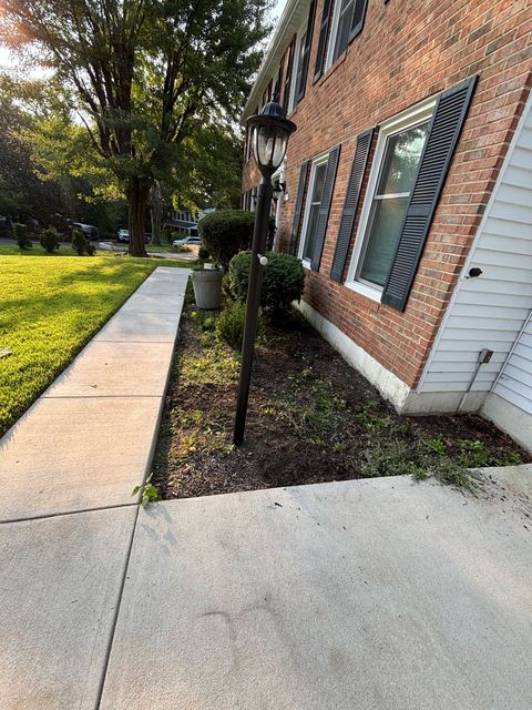 Brick building exterior with sidewalk, grass lawn, shrubs, and windows with shutters