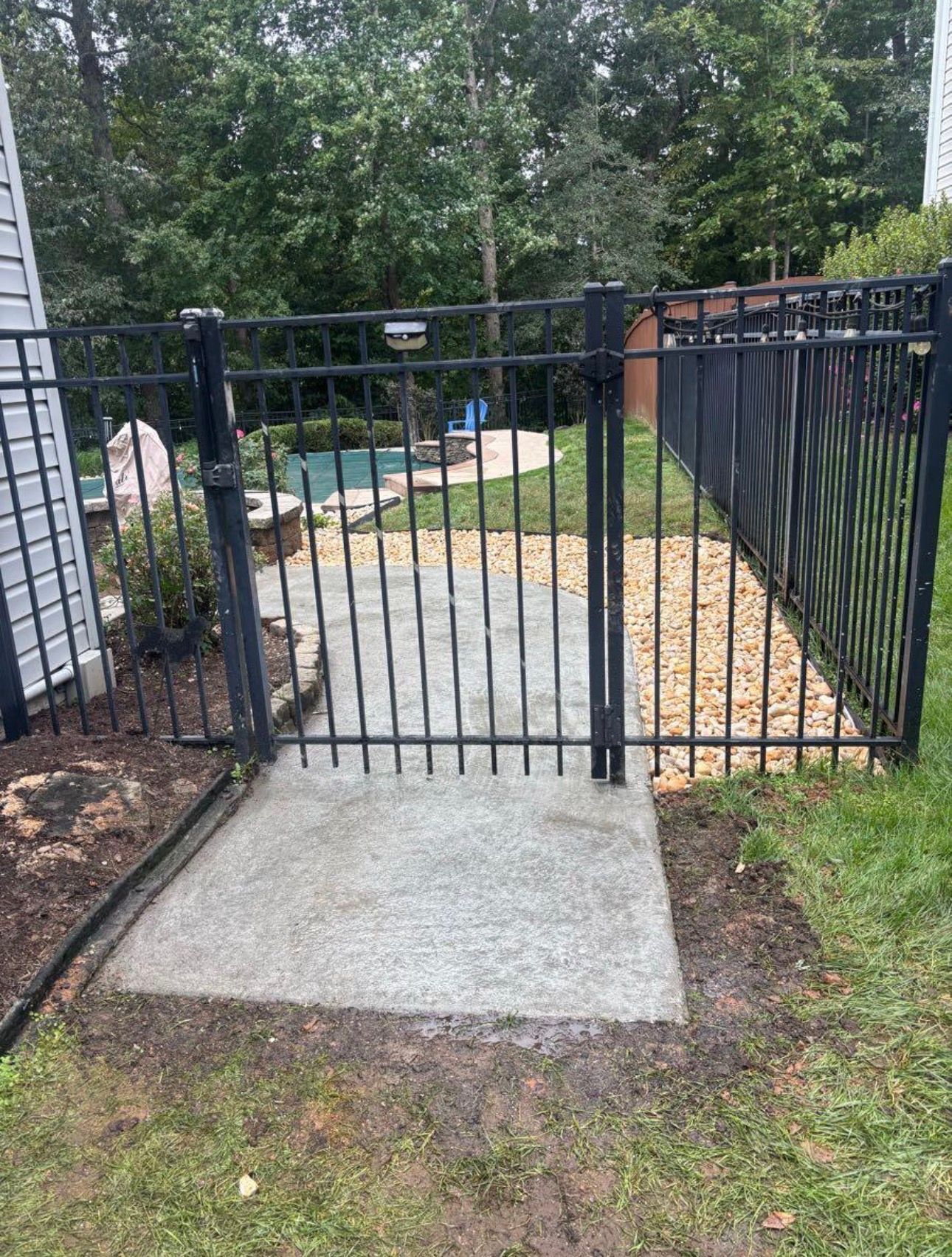 Black metal gate at the end of a concrete walkway in a grassy yard.