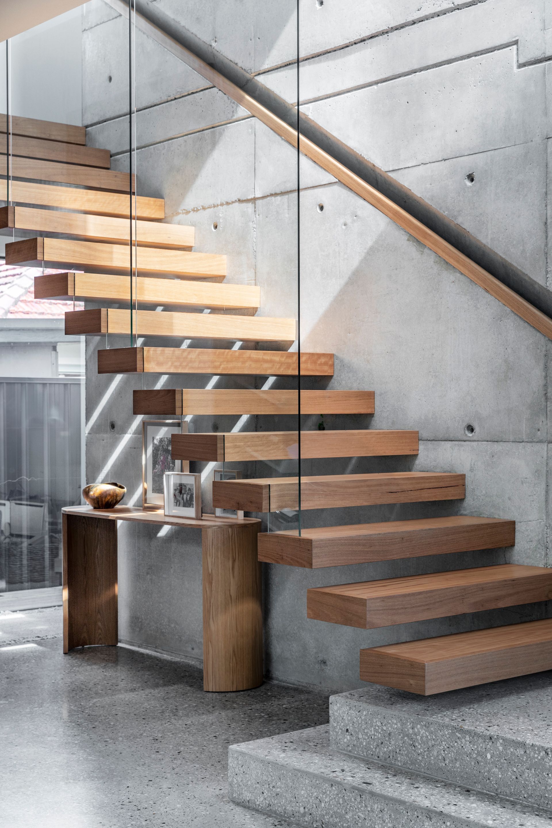 Wooden floating staircase against a concrete wall, glass railing, small wooden table with decor — Make The Mark Building Services in Illawarra, NSW
