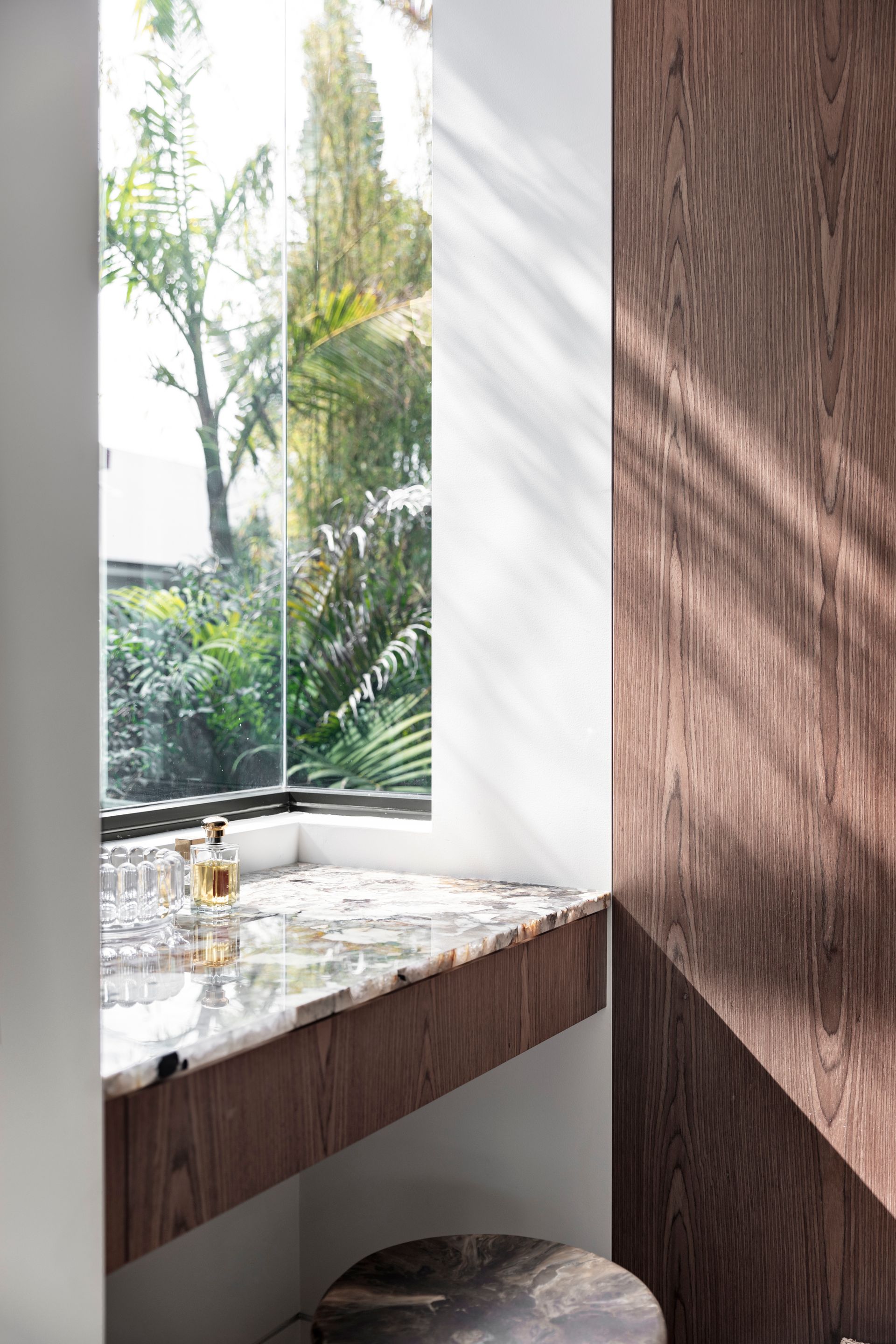 Window with a stone countertop, perfume bottles, and wooden paneling. Sunlight casts shadows on the wall — Make The Mark Building Services in Illawarra, NSW