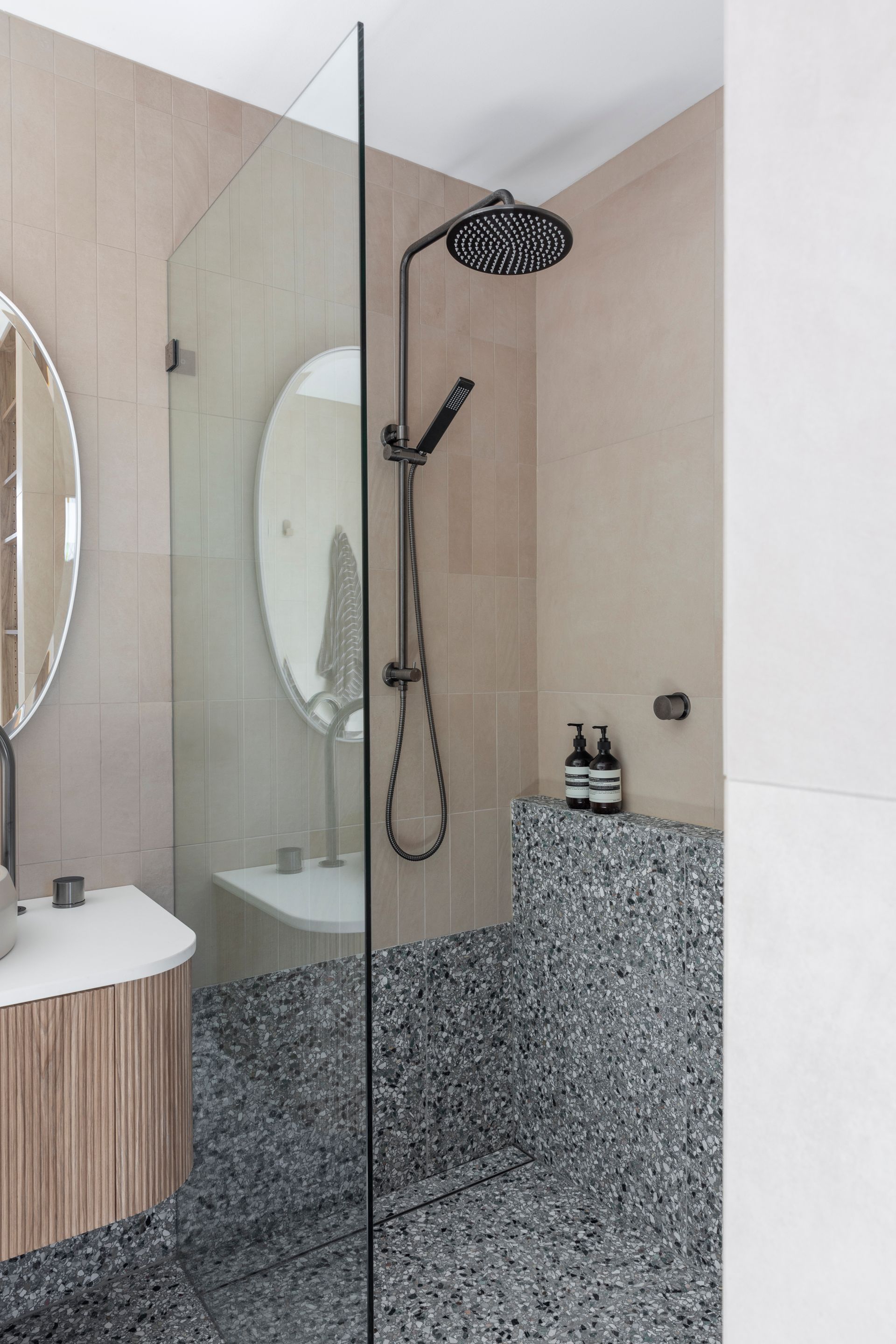 Shower with glass wall, black hardware, gray speckled floor, and beige walls — Make The Mark Building Services in Illawarra, NSW