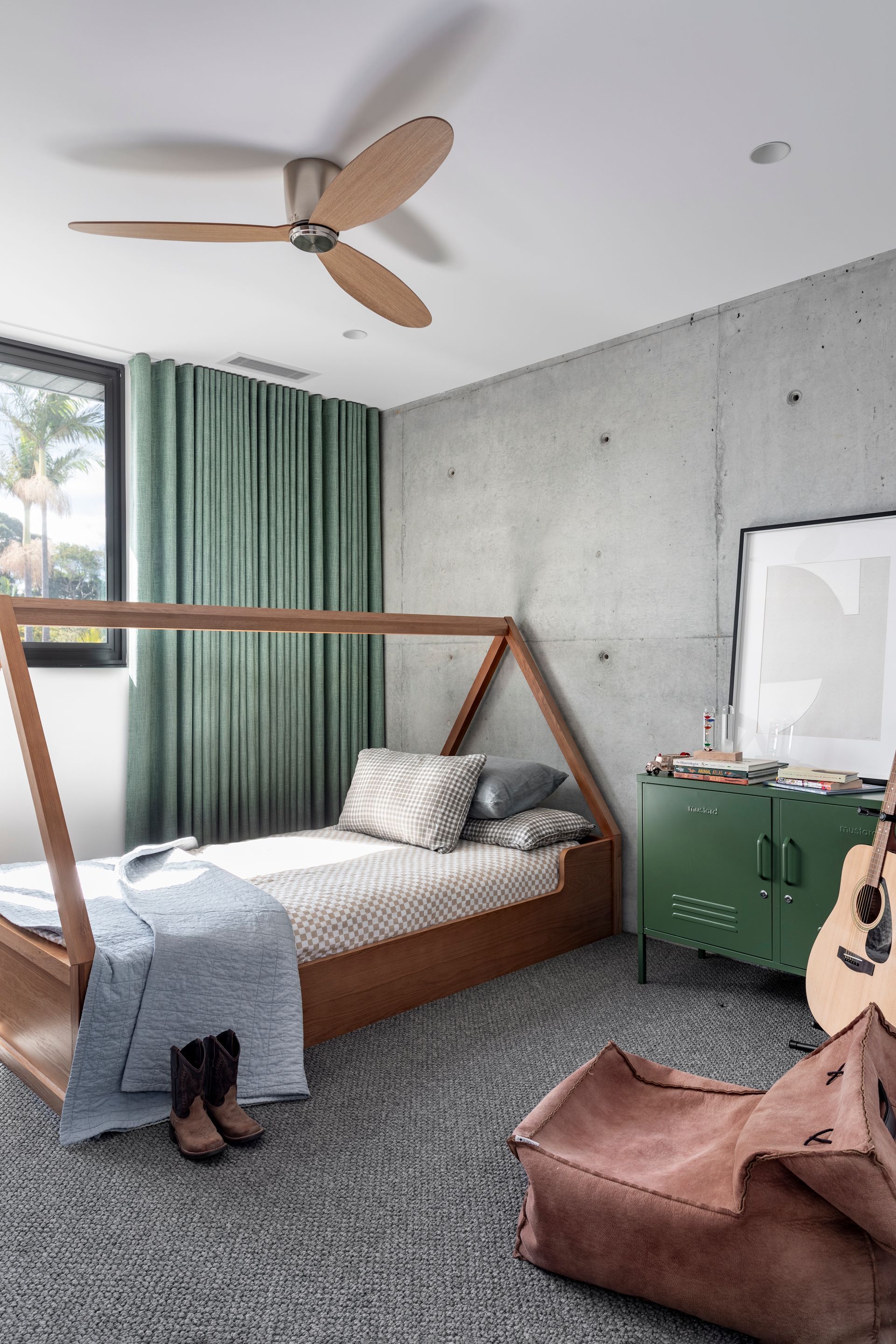 Bedroom with a wooden bed frame, concrete wall, green curtains, and a green cabinet — Make The Mark Building Services in Illawarra, NSW
