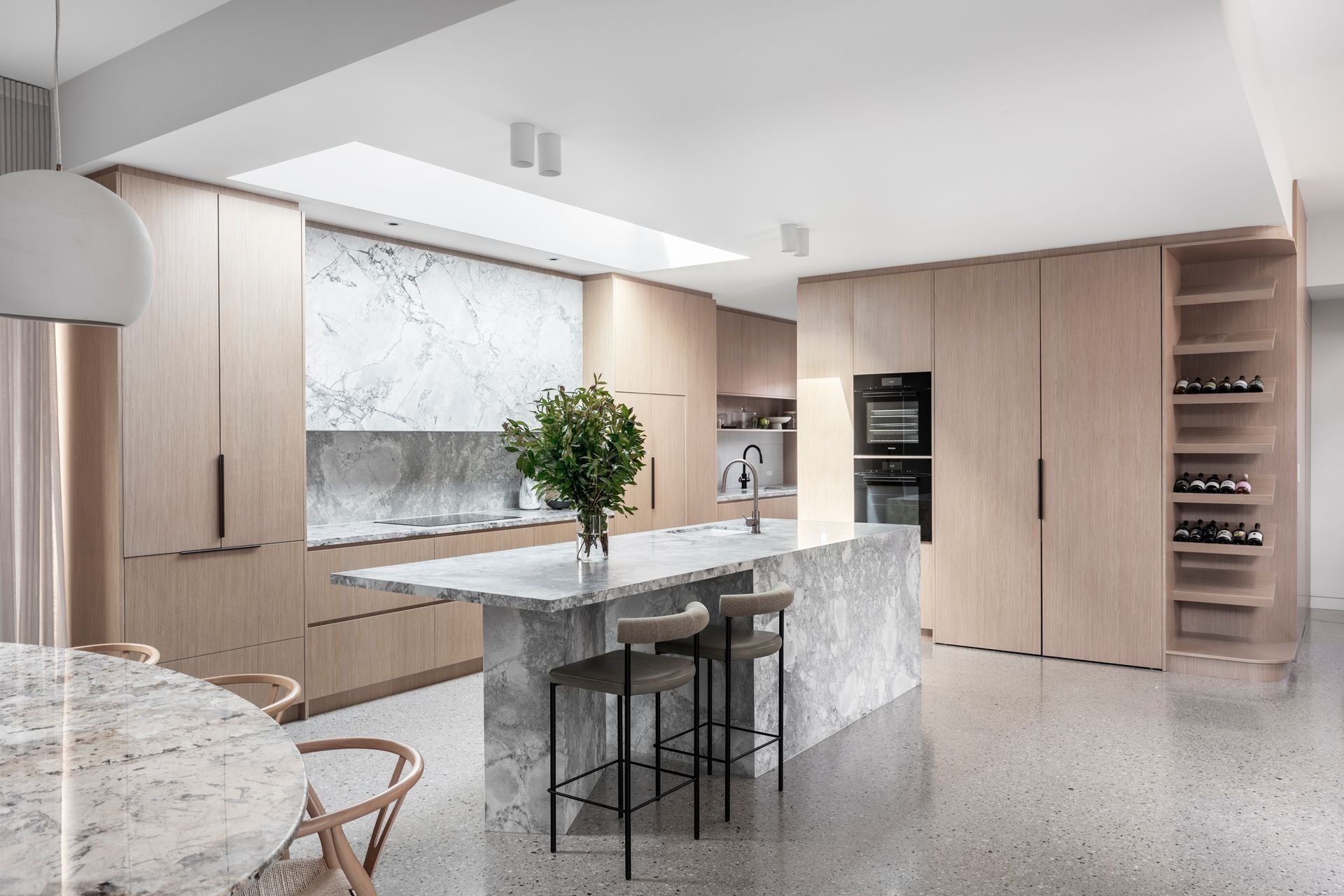 Modern kitchen with light wood cabinets, marble island and backsplash, and a large skylight — Make The Mark Building Services in Illawarra, NSW