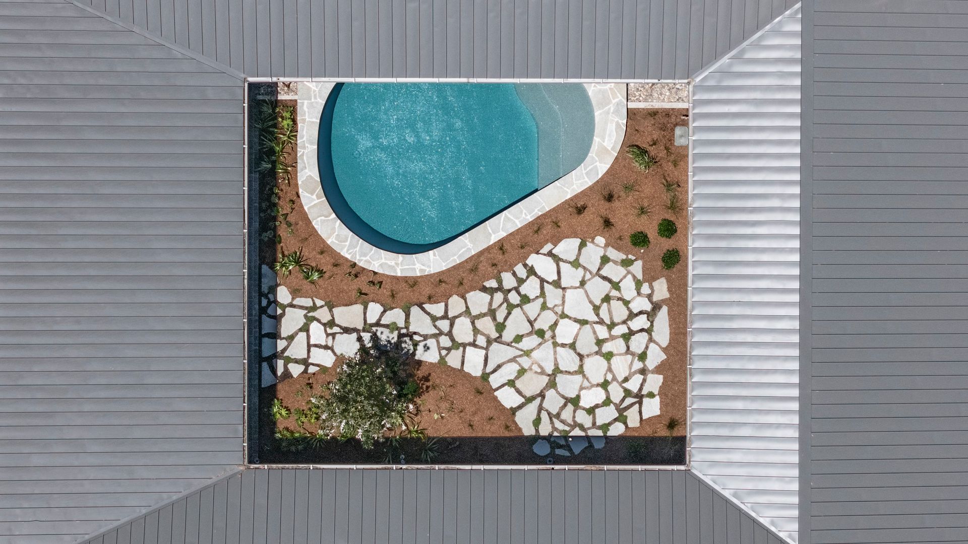 Overhead view of a courtyard with a blue pool, stone patio, and surrounding gray building — Make The Mark Building Services in Illawarra, NSW