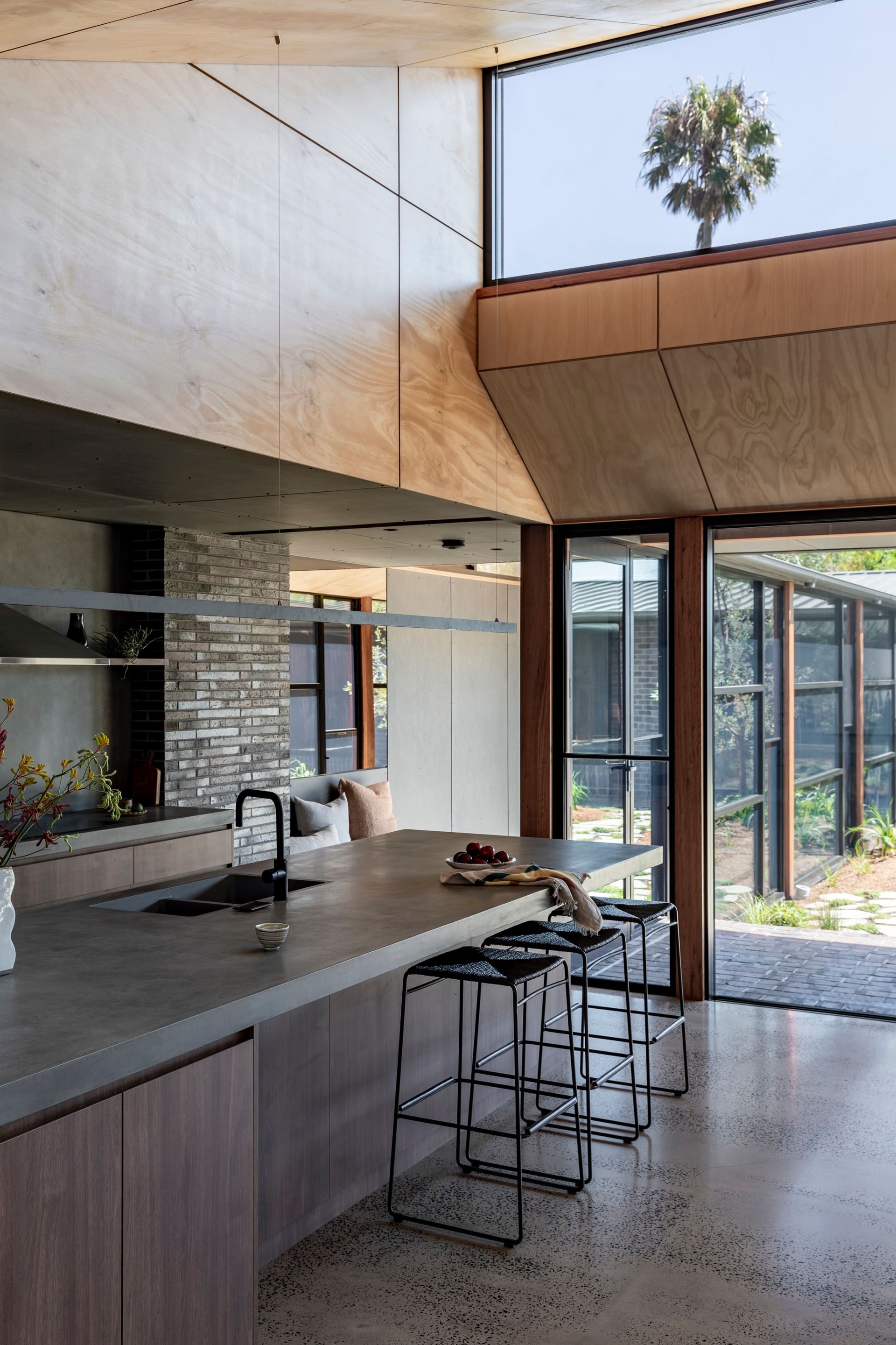 Modern kitchen with concrete countertop, wood cabinets, and large window overlooking a palm tree — Make The Mark Building Services in Mangerton, NSW