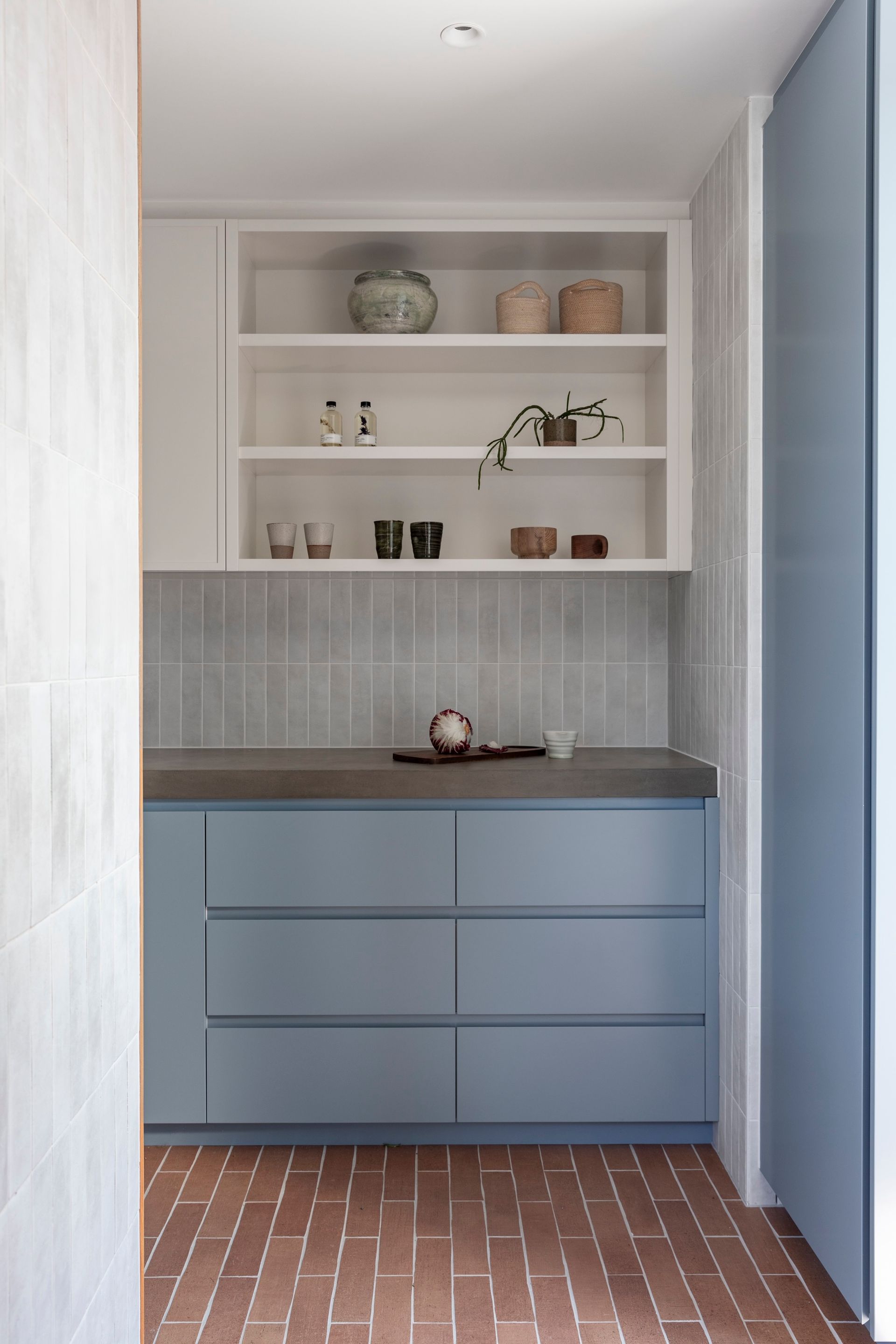 Blue cabinets, white shelves, gray tile, and terracotta brick floor in a kitchen area — Make The Mark Building Services in Illawarra, NSW