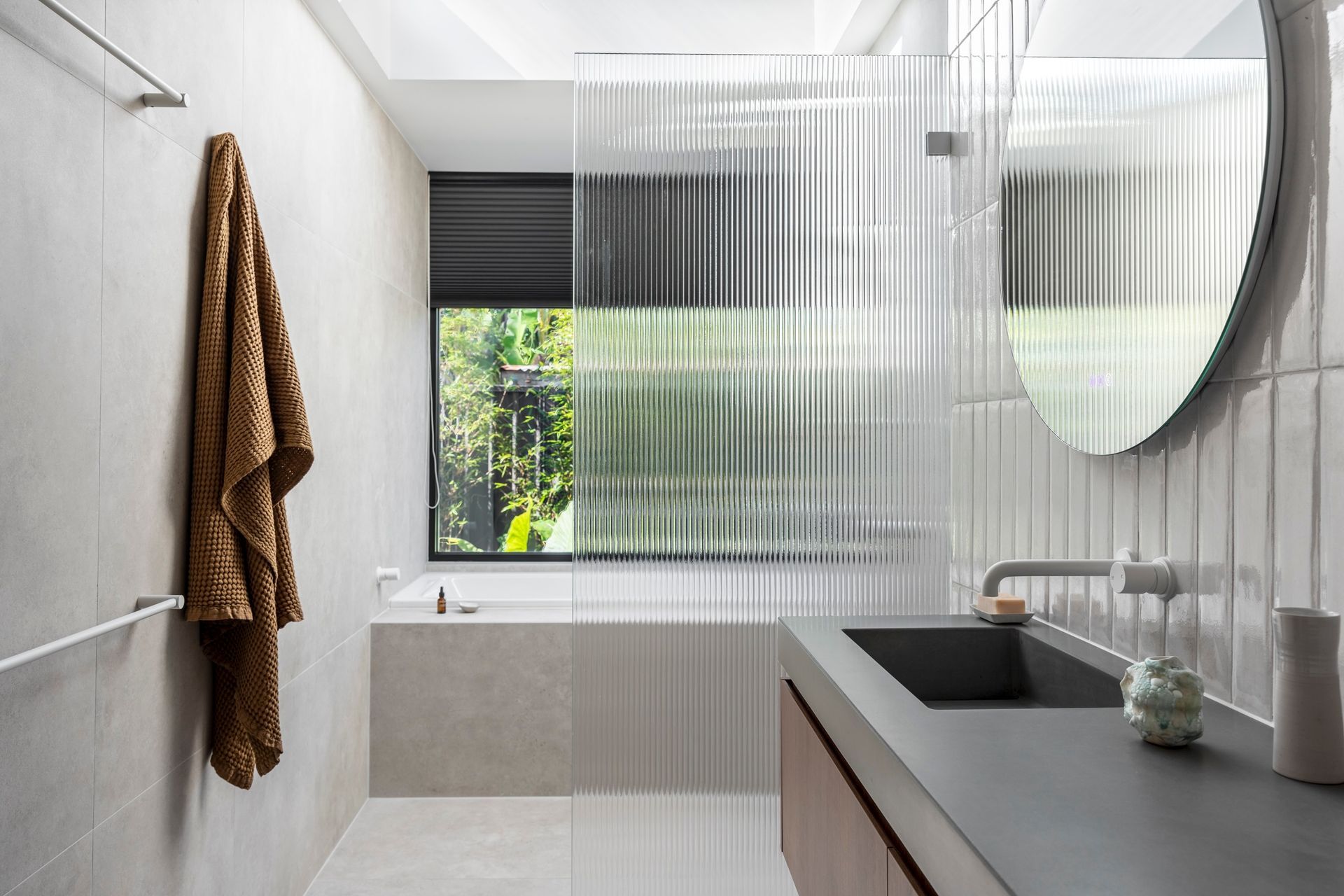 Modern bathroom with a bathtub, large mirror, and dark countertop with a sink. A brown towel hangs on a nearby rack — Make The Mark Building Services in Illawarra, NSW