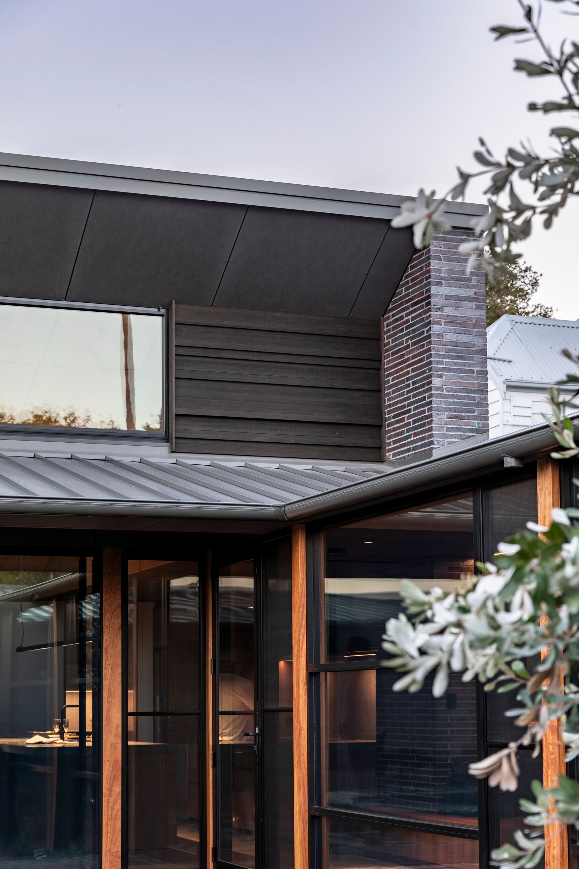 Exterior of a modern home with a dark gray roof, wood siding, brick chimney, and large windows — Make The Mark Building Services in Illawarra, NSW