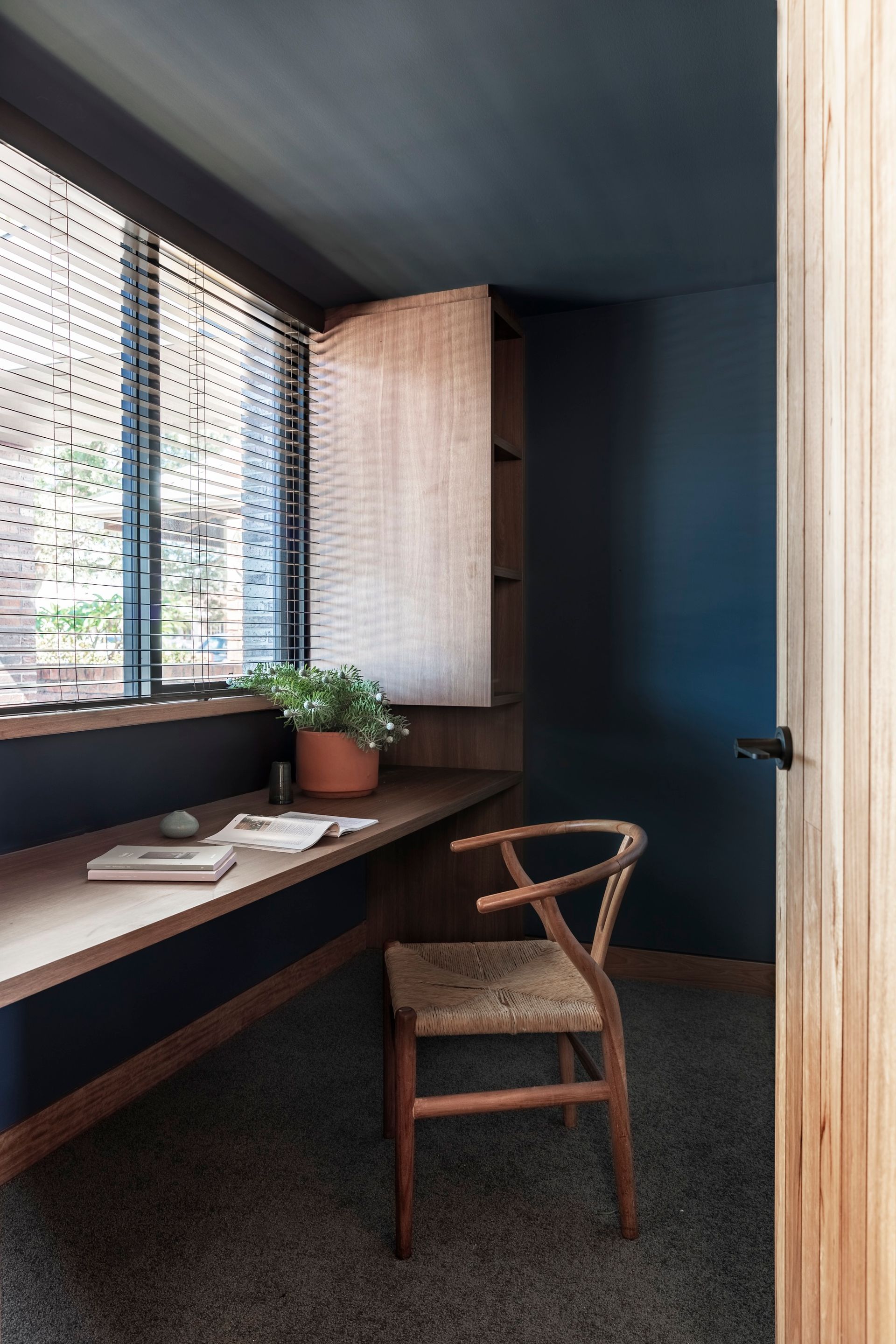 Cozy home office with built-in desk, navy walls, wood chair, and sunlight through blinds — Make The Mark Building Services in Illawarra, NSW