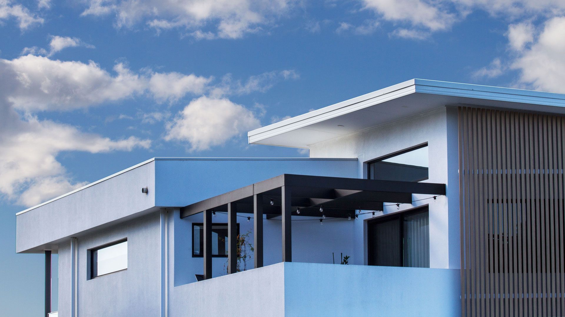 Modern white house with a deck and dark pergola against a blue sky with clouds  — Make The Mark Building Services in Illawarra, NSW