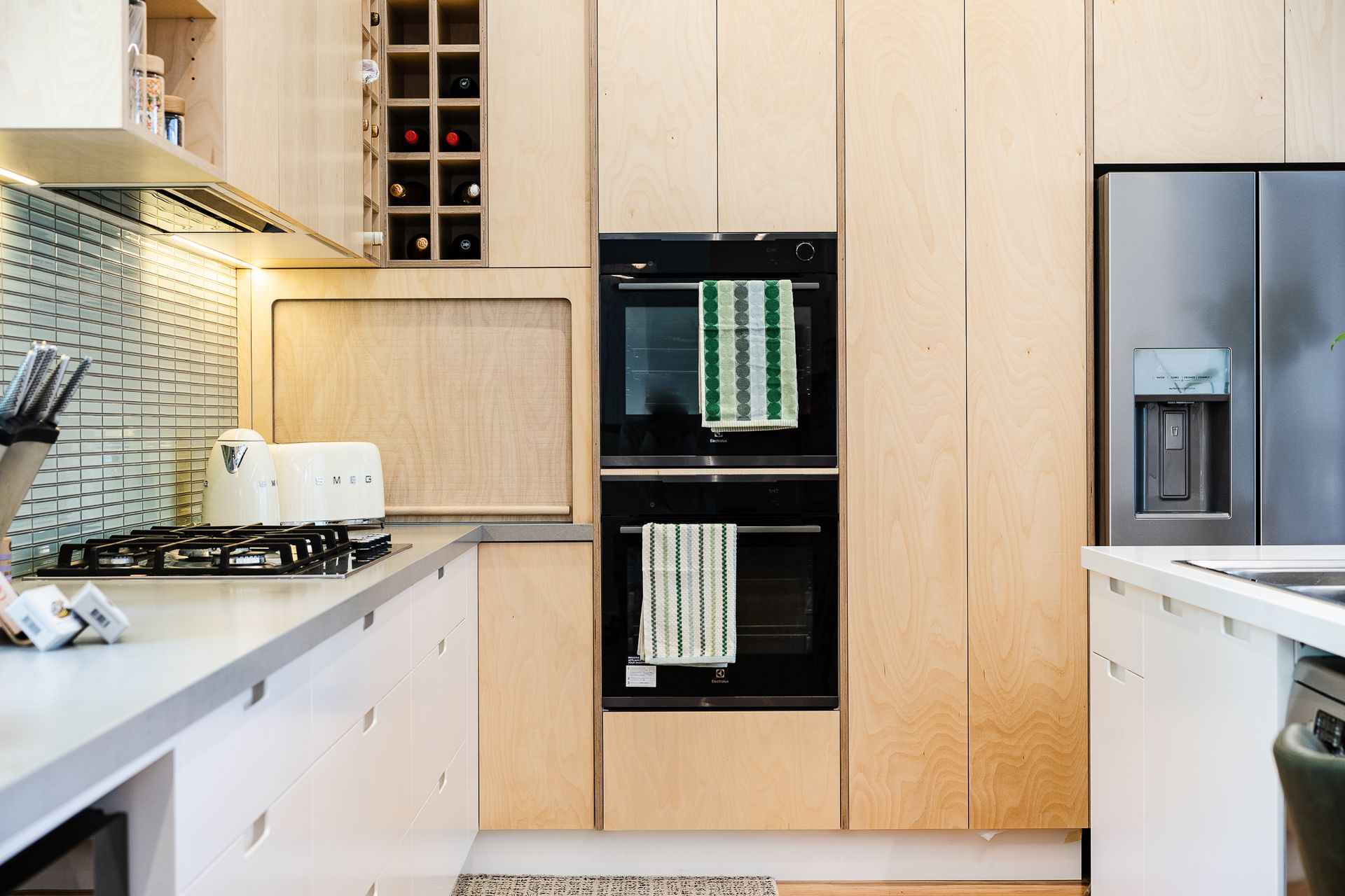 Modern kitchen with light wood cabinets, double oven, and stainless steel refrigerator - Make The Mark Building Services in Mangerton, NSW