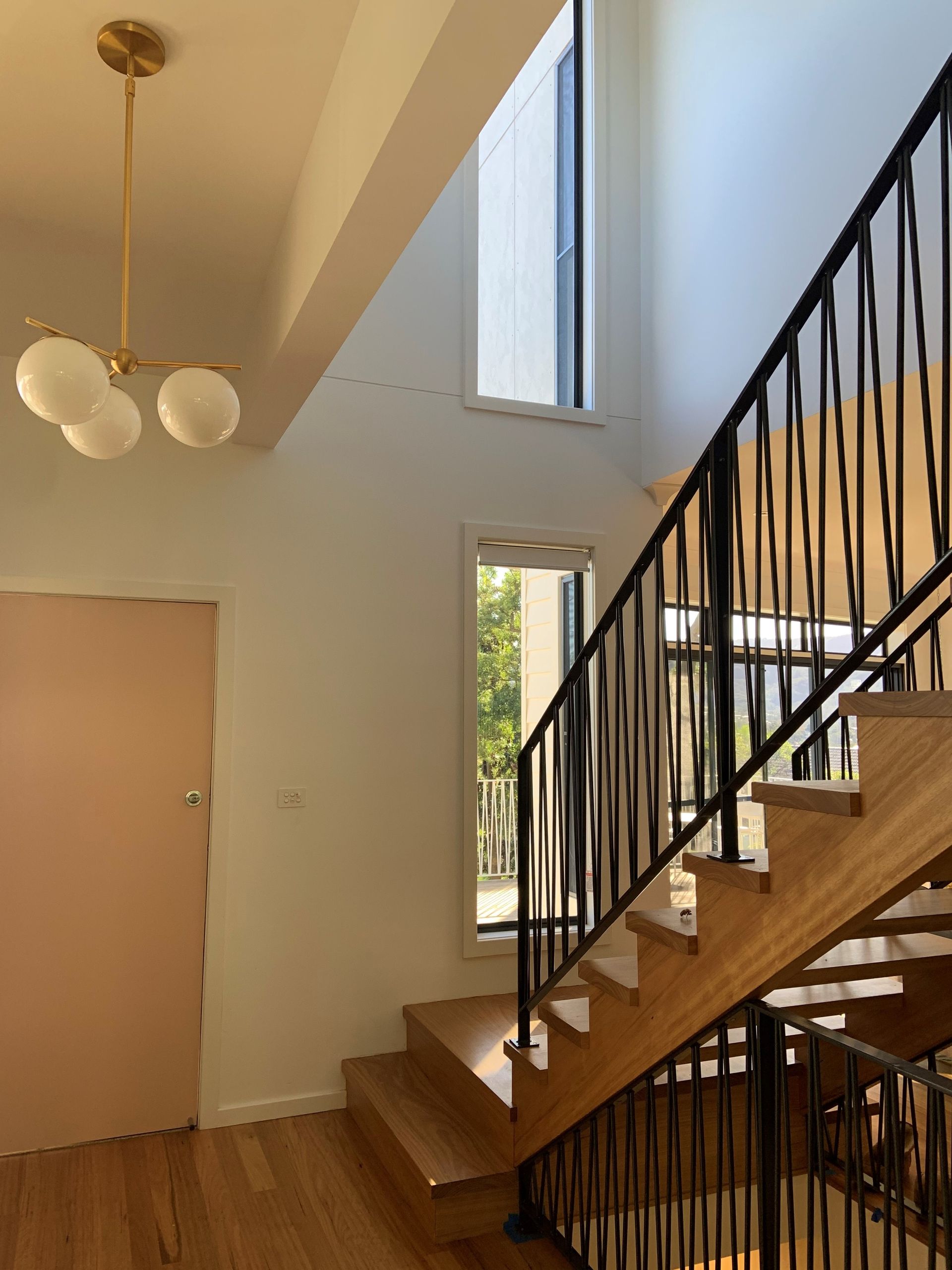 Staircase with wooden steps and black railing, light fixture, and window. Pink door on the left - Make The Mark Building Services in Mangerton, NSW