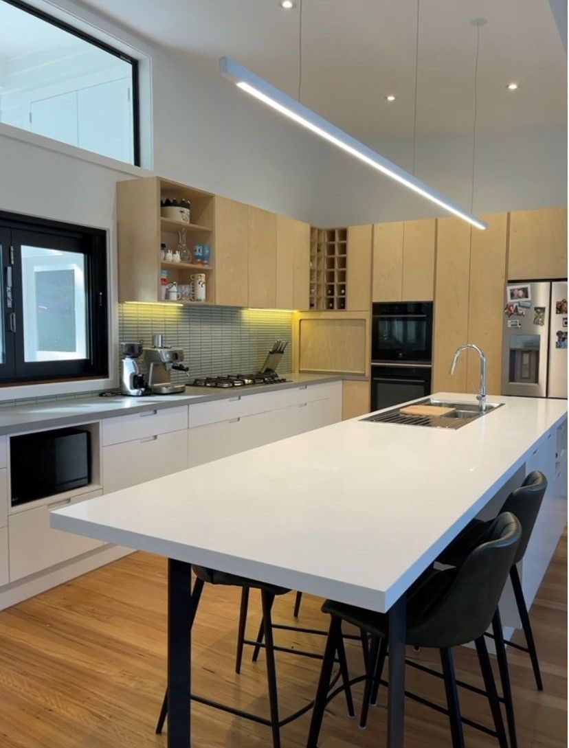 Modern kitchen with white countertops, light wood cabinets, and a long linear light fixture - Make The Mark Building Services in Mangerton, NSW