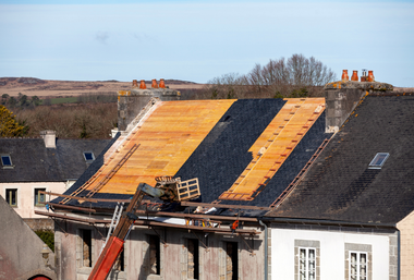 Roof under repair with exposed wooden sheathing and ladders on a house.