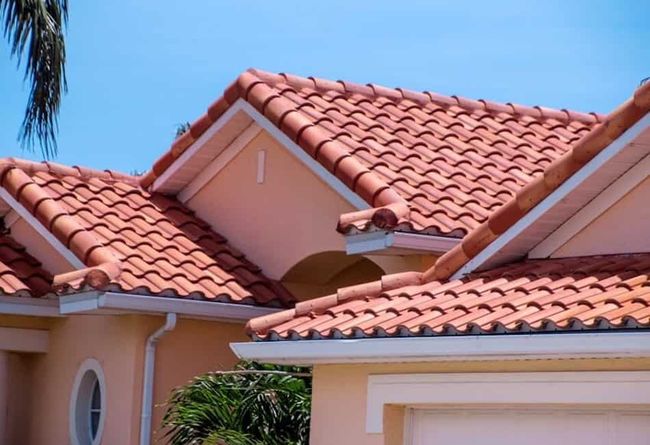 Worker in orange helmet kneeling on a tiled roof, inspecting or repairing it.