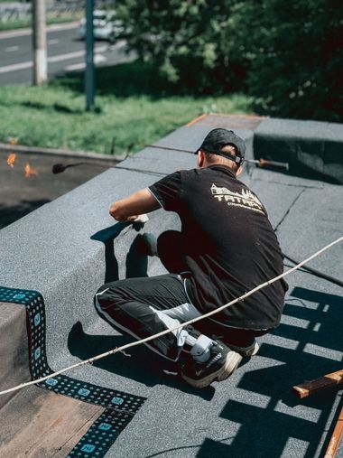 Person crouching on a rooftop, working near a rope and dark shingles