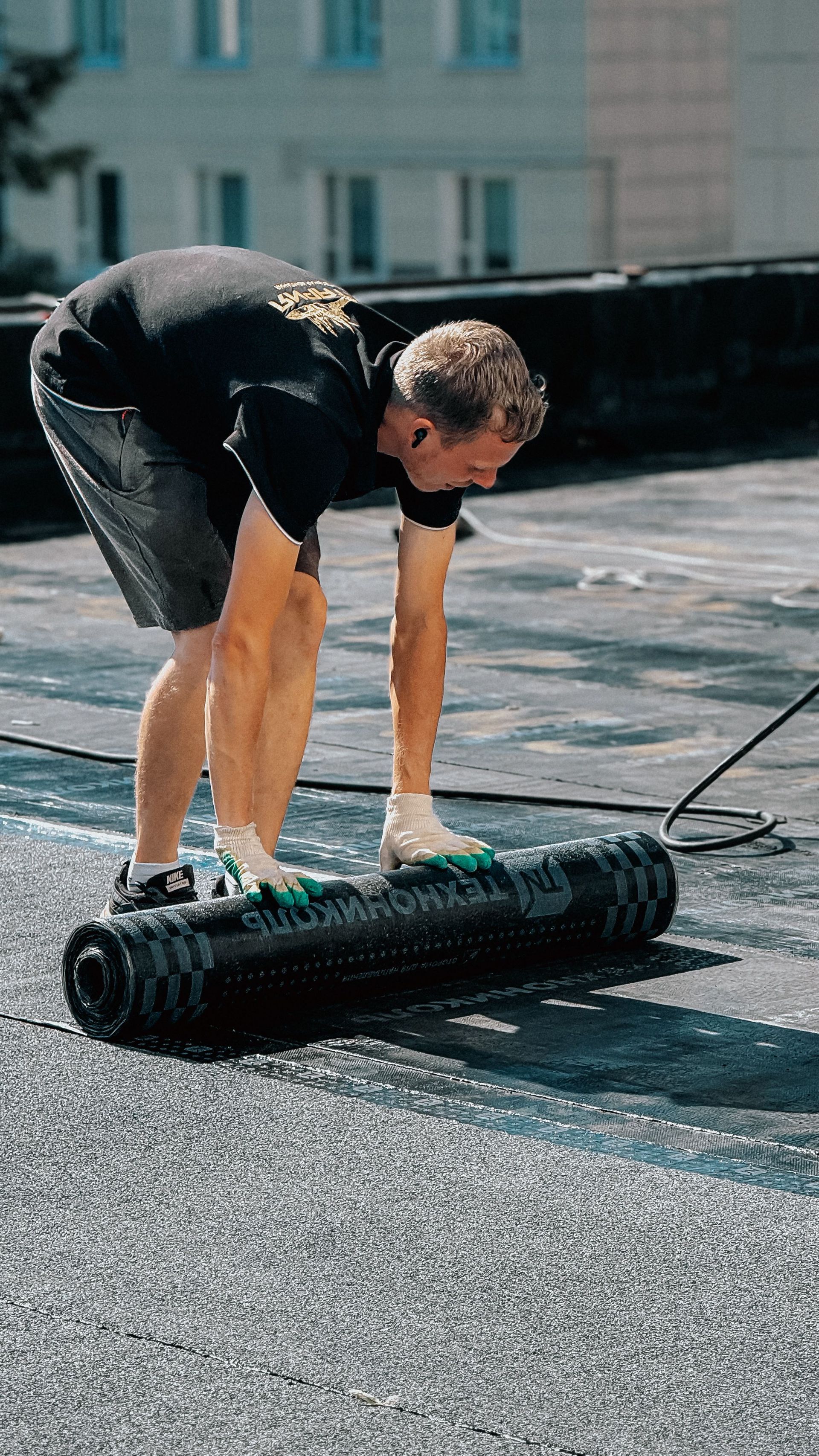 Person lifting a rolled black mat on a rooftop under bright daylight