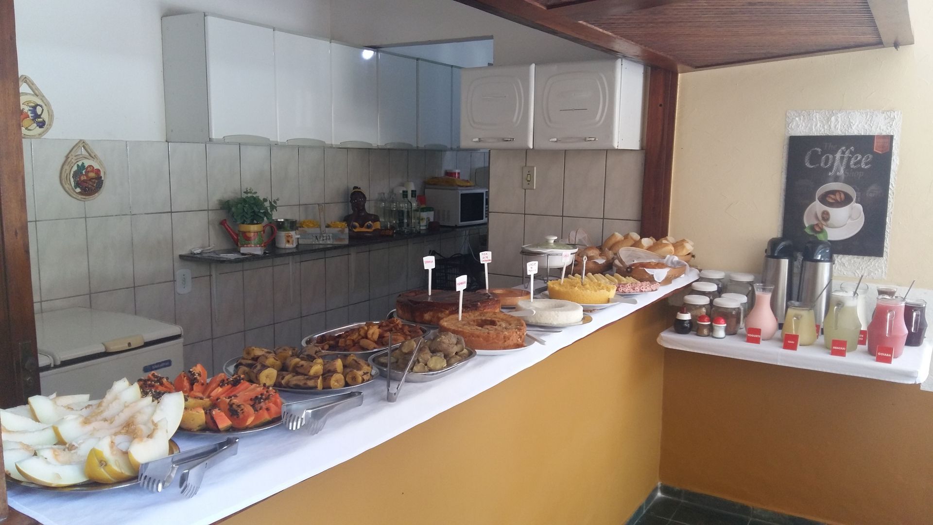 Uma cozinha com um longo balcão cheio de comida e bebidas.-Pousada-A-Flor-Da-Terra