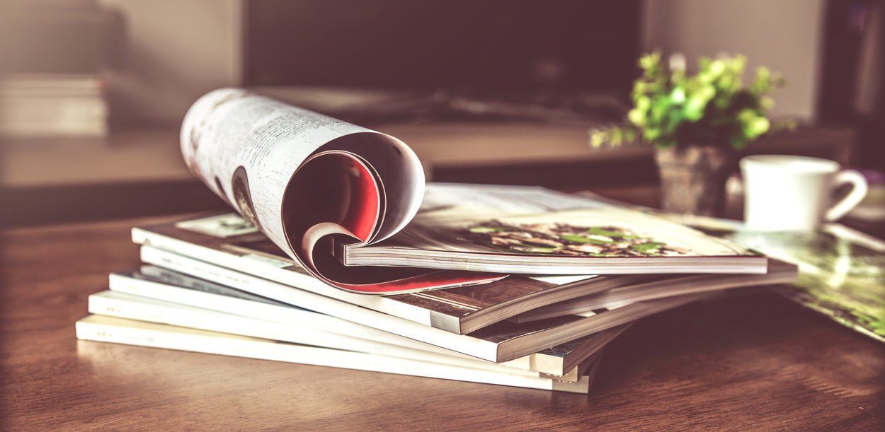 A stack of magazines sitting on top of each other on a wooden table.