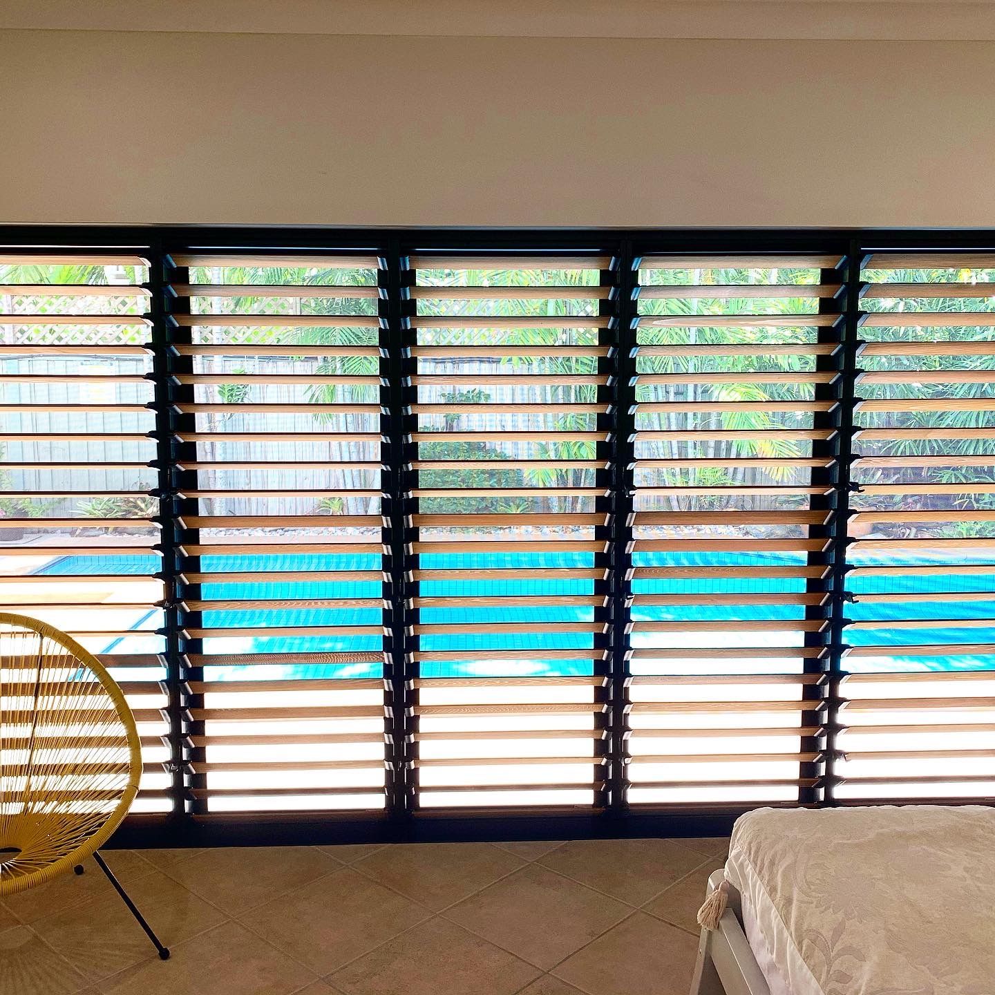 A bedroom with a view of a swimming pool through a window with shutters.