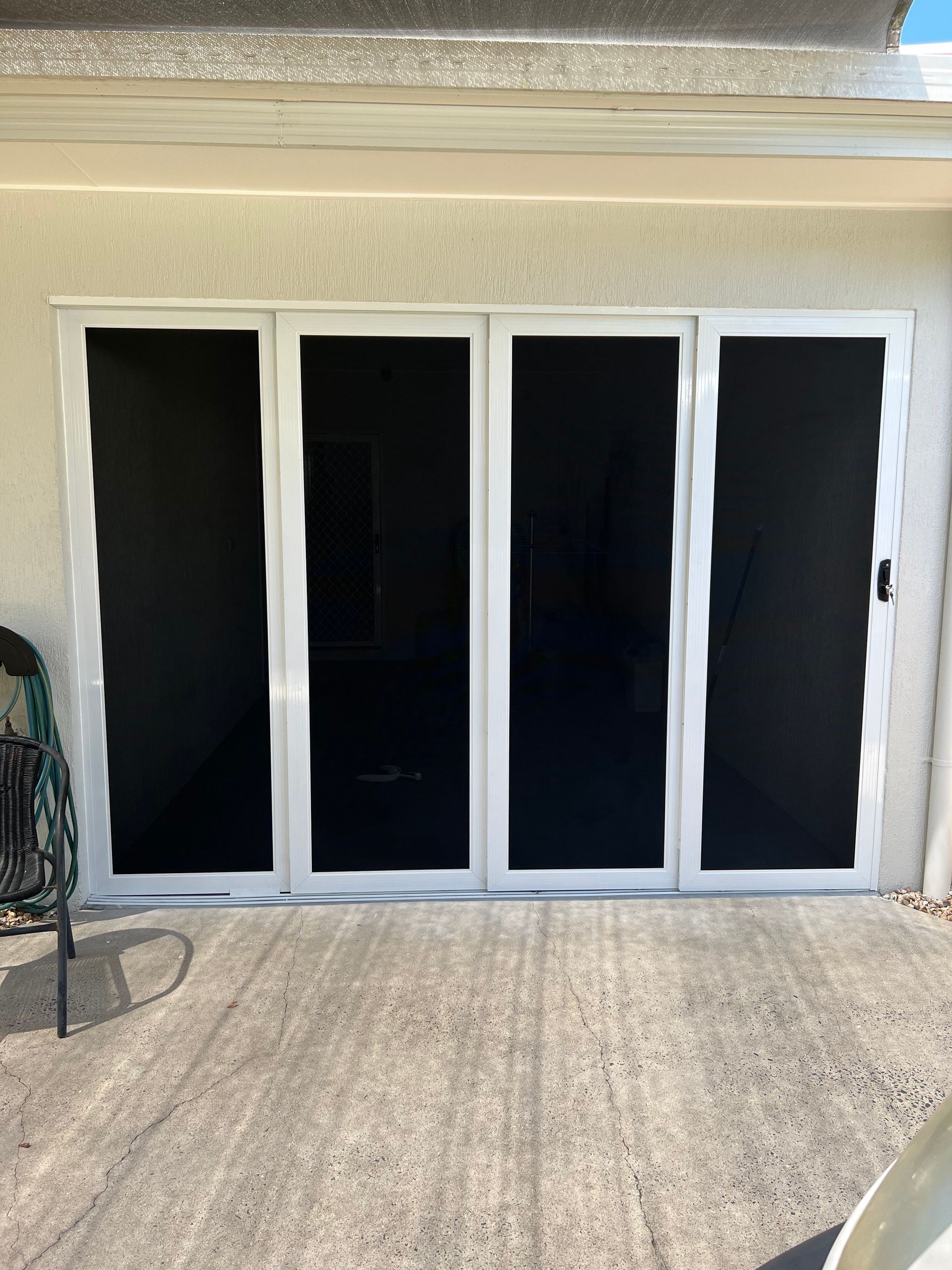 A white sliding glass door with black screens on a patio.