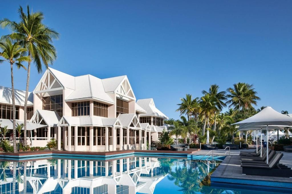 A large white house with a swimming pool in front of it surrounded by palm trees.