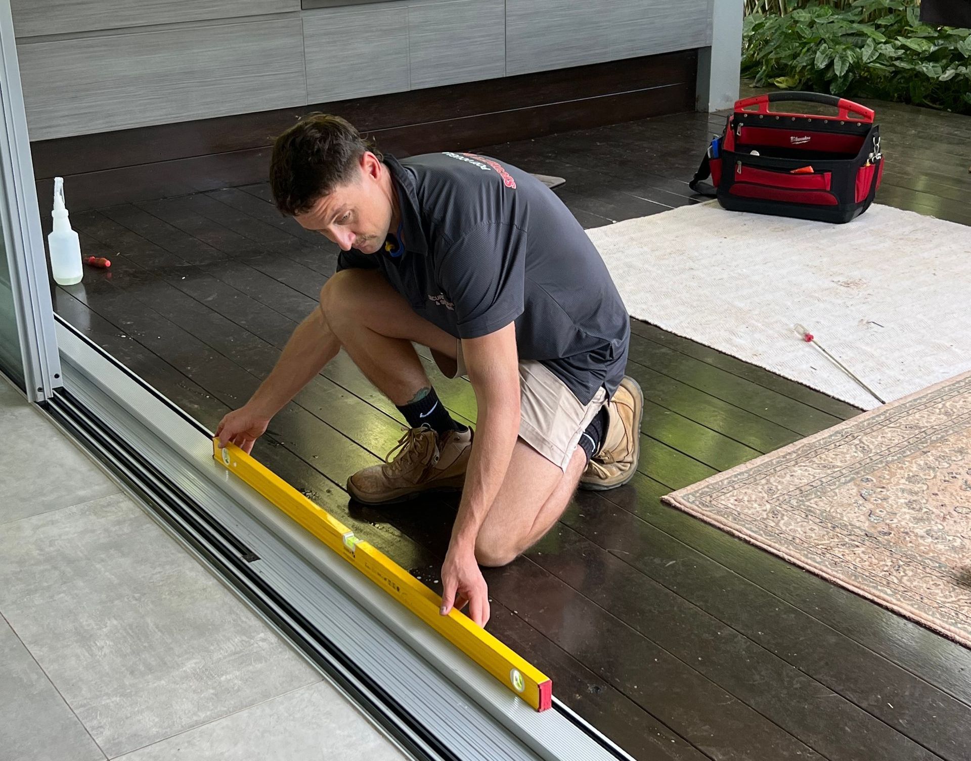 A man is kneeling down on the floor using a level.