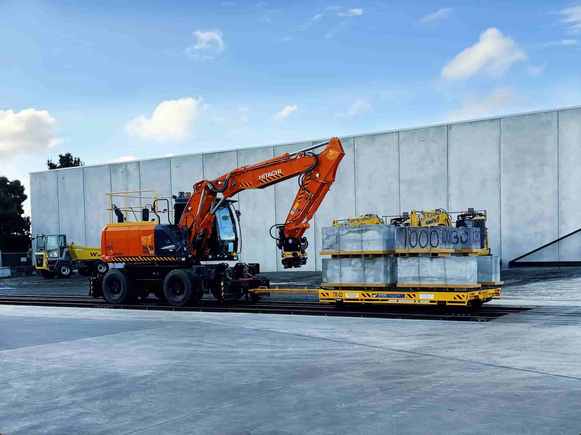 Road-rail wheeled excavator towing a loaded test trailer during braking and performance testing on a rail test track.