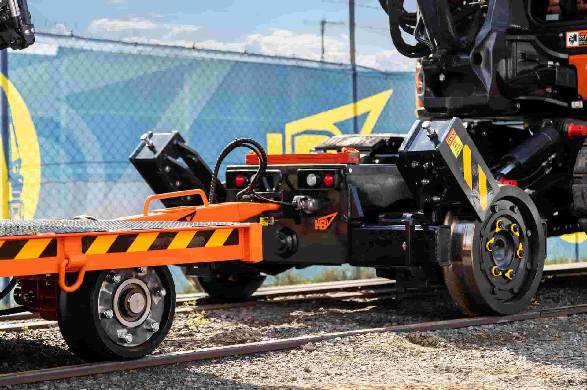 Excavator mounted on a rail guidance trailer undergoing towing and performance testing on a rail test track.
