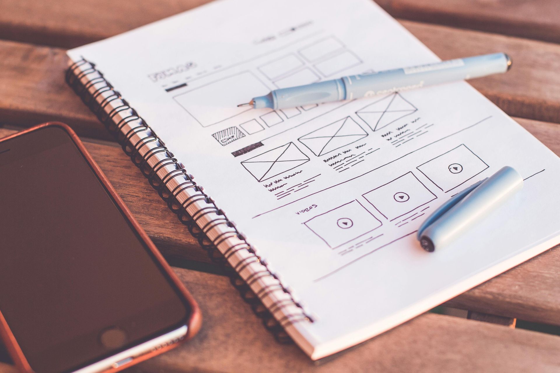 Notebook with website wireframes, pen, and smartphone on a wooden table. 