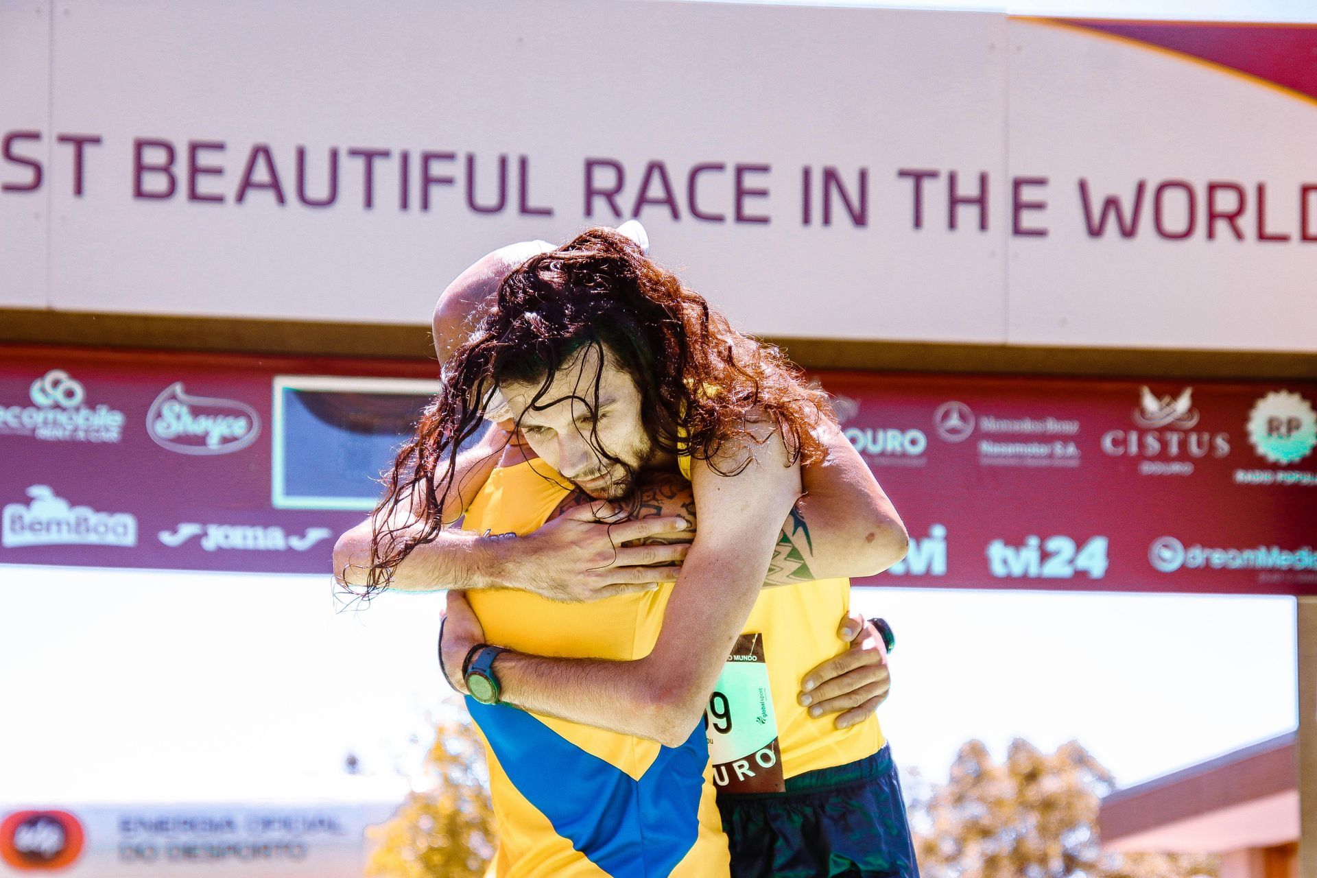 Man hugging a woman after a race; they are smiling and celebrating under a banner that reads .