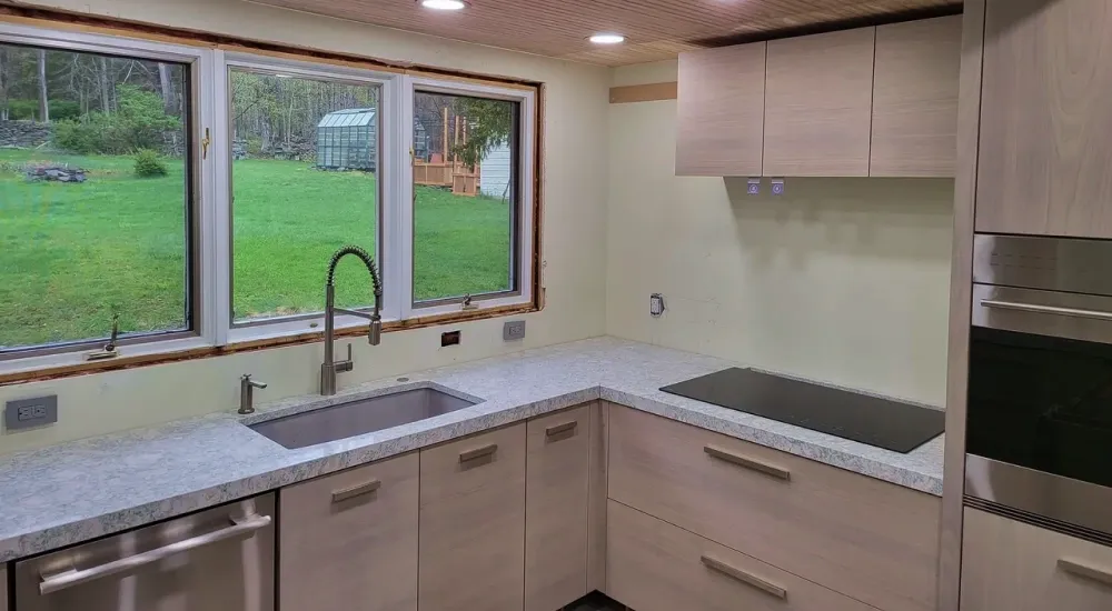 A kitchen with a sink , stove , dishwasher , and a large window.