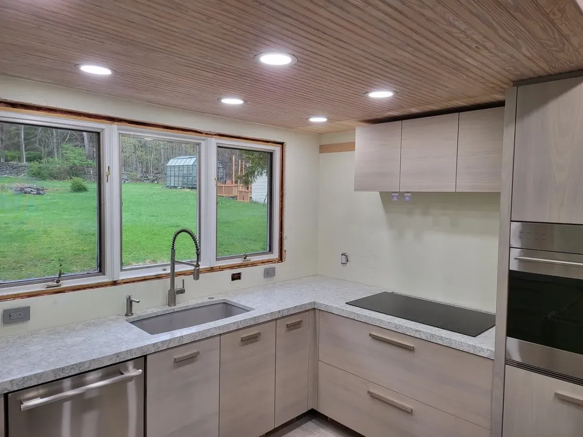 A kitchen with a sink , stove , dishwasher , and a large window.