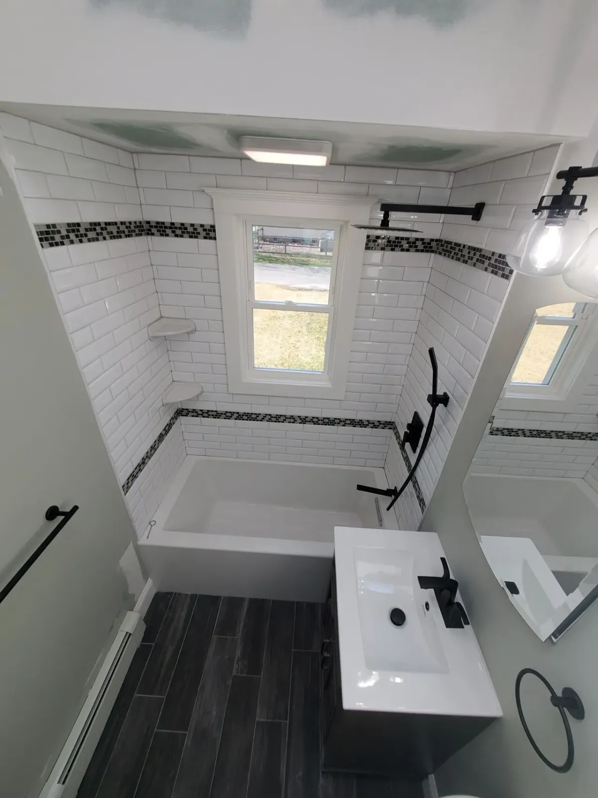 A bathroom with a tub , sink , mirror and window.