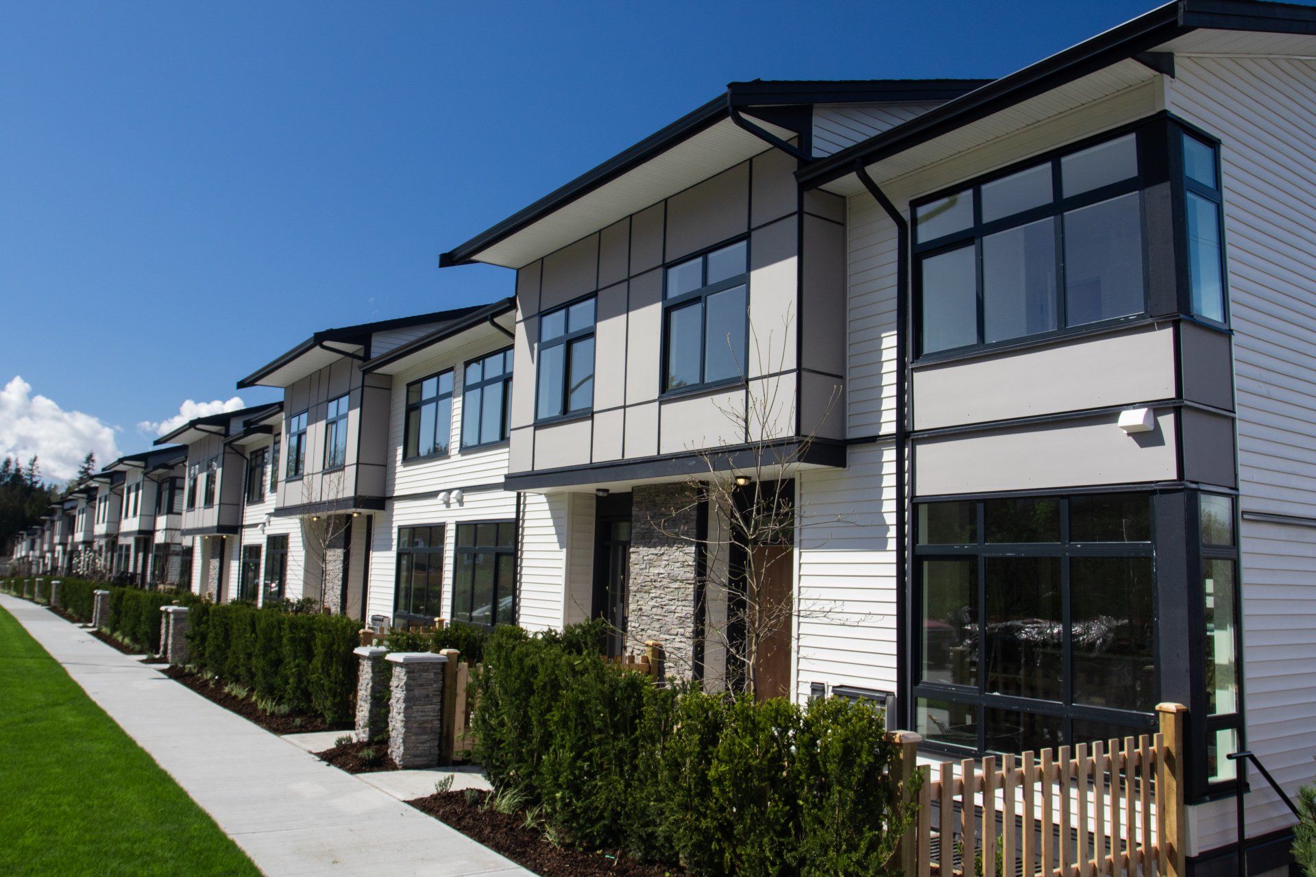 Rangée de maisons de ville modernes avec revêtement gris et blanc, fond de ciel bleu.