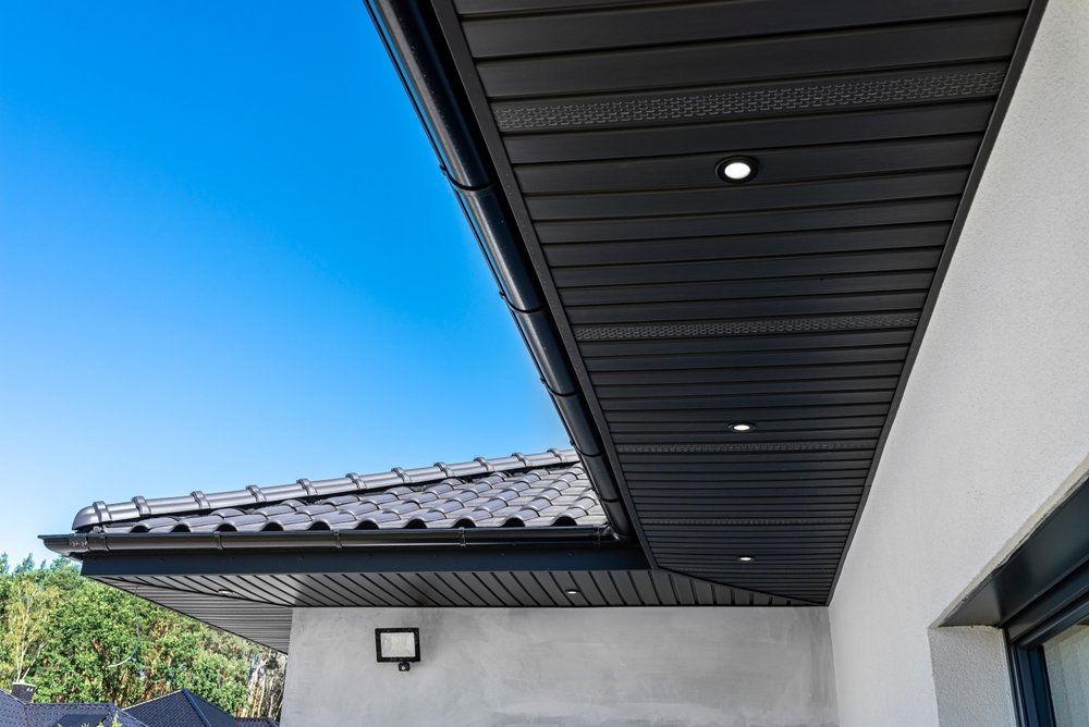 Soffite noir avec lumières encastrées et toit en tuiles foncées contre un ciel bleu.