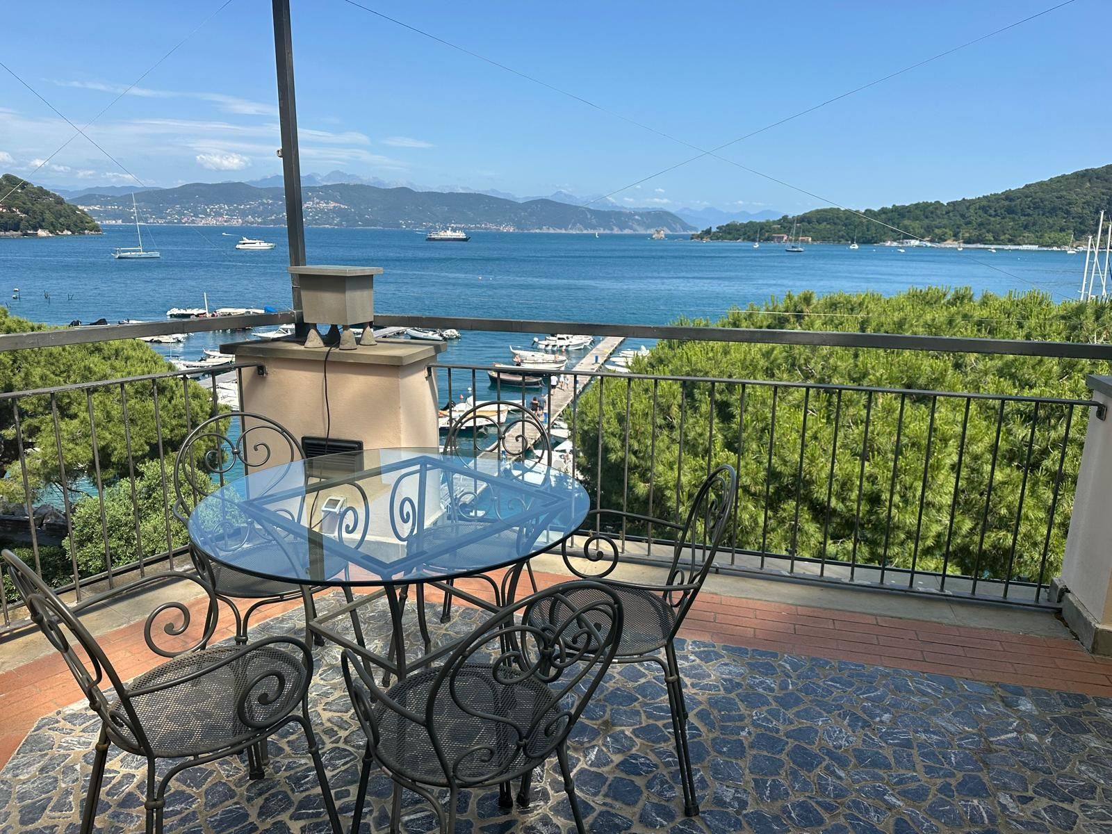 Balcone con tavolo e sedie con vista sul porto con barche e sul mare blu.